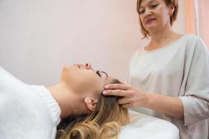 Healer performing by lightly touched set of 32 points of access bars on young woman head, stimulating positive change thoughts and emotions in salon. Alternative medicine concept photo