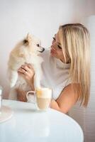 Beautiful blonde young woman with Pomeranian spitz dog and cup of coffee in home kitchen photo