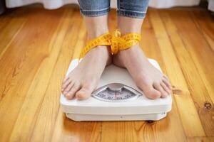 Womens bare feet tied with measuring tape stand on scales on wooden floor photo