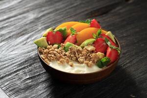 A Bowl of Homemade Granola with Yogurt and Fresh Avocado, Strawberry, and Apricot. photo