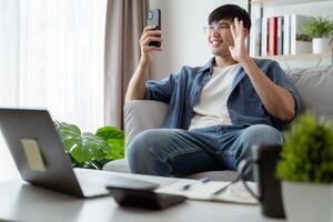 alegre contento joven asiático hombre utilizando inteligente teléfono para en línea vídeo conferencia llamada hablando felizmente. foto