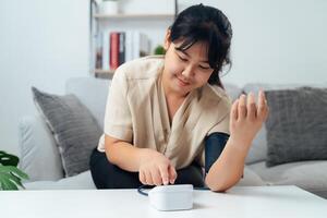 A woman is sitting on a couch and using a blood pressure monitor photo