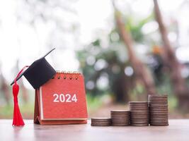 Study goals, 2024 Desk calendar with graduation hat and stack of coins. The concept of saving money for education, student loan, scholarship, tuition fees and manage time to success graduate. photo