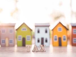 Wooden words with the TAX on stack of coins with Miniature house background. The concept of payment tax for house, Property investment, House mortgage, Real estate photo