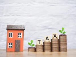 Miniature house and Wooden blocks with the word TAX on stack of coins. The concept of payment tax for house, Property investment, House mortgage, Real estate photo