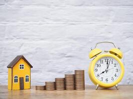 amarillo alarma reloj, miniatura casa y apilar de monedas el concepto de ahorro dinero para casa, gestionar hora a éxito, propiedad inversión, casa hipoteca, real inmuebles foto