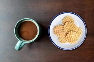 Top view mocha coffee in green cup and many waffle on dish on wooden table photo