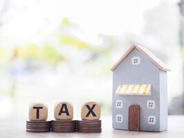 Miniature house and Wooden blocks with the word TAX on stack of coins. The concept of payment tax for house, Property investment, House mortgage, Real estate photo