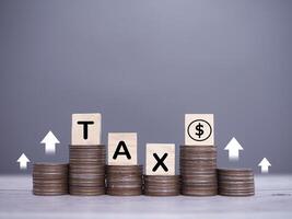 Wooden blocks with the word TAX and dollar coin icons, Stack of coins with arrow rising up icons. The concept about saving money and manage time to paying tax photo