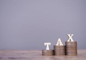 Wooden words with the TAX on stack of coins. The concept about saving money and manage time to paying tax photo