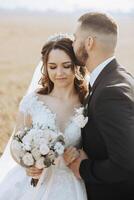 A young bride and groom tenderly embrace in the rays of the autumn sun. Tender and beautiful young girl bride. A man kisses his beloved. Against the background of a beautiful garden photo