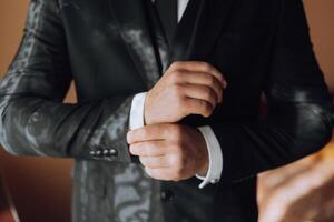 joven sonriente hombre abotonarse arriba su chaqueta en el Mañana antes de el boda. de cerca de un hombre en un negocio traje. empresario pone en un traje. un hombre sujeta el botones en su chaqueta. foto