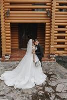 Handsome groom and charming bride stay together near modern wooden house in park photo