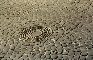 Old metal sewer hatch in the middle of the road, laid out of a smooth paving stone photo