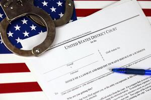 District court Notice of the lawsuit and request to waive service of a summons. Papers with handcuffs and blue pen on United States flag photo