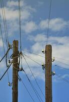 Old wooden electric pole for transmission of wired electricity on a background of a cloudy blue sky. Obsolete method of supplying electricity for later use photo