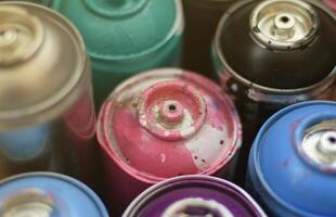 Large number of used colorful spray cans of aerosol paint lying on the treated wooden surface in the artist's graffiti workshop close up. Dirty and stained cans for art photo