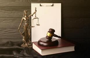 Lady justice or justitia the Roman goddess of Justice. Statue on brown book with judge gavel on blank paper background with copyspace. Concept of judicial trial, courtroom process and lawyers work photo