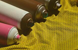 Several used aerosol paint sprayers lie on the sports shirt of a basketball player made of polyester fabric. The concept of youth street art, active sports and eventful lifestyle photo