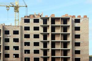 View of a large construction site with buildings under construction and multi-storey residential homes. Tower cranes in action on blue sky background. Housing renovation concept photo