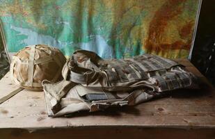 A military helmet of a Ukrainian soldier with a heavy bulletproof vest on wooden table in checkpoint dugout photo