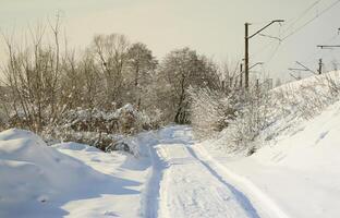 The road that lies parallel to the railway line is covered with snow on a sunny day after a heavy snowfall photo