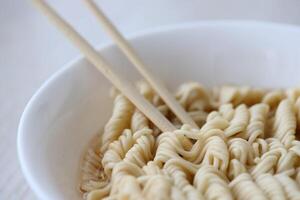 Bowl of instant cooking noodles with wooden chopsticks on white wooden table photo