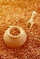 Background image of a large pile of buckwheat, in the middle of which lies a small jug and a wooden spatula for cereals photo