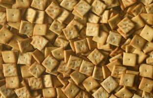 A lot of small cookies are square shaped. A pattern of a yellow salt cracker. Background image with salted pastry photo