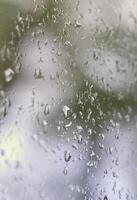 una foto de gotas de lluvia en el cristal de la ventana con una vista borrosa de los árboles verdes florecientes. imagen abstracta que muestra las condiciones meteorológicas nubladas y lluviosas