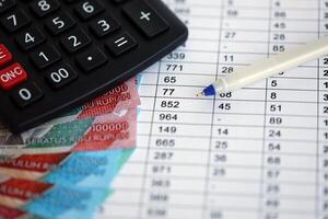 Business calculations with indonesian rupiah money bills and calculator with pen on office table photo