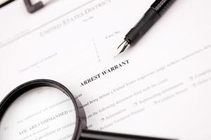 District Court Arrest Warrant court papers on A4 tablet lies on office table with pen and magnifying glass photo