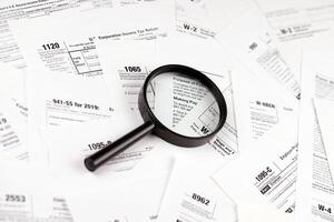 Magnifying glass lying over heap of paper documents. Investigation and financial audit photo