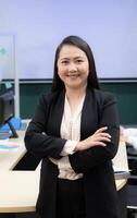 A woman in a black suit and white shirt is smiling and standing with her arms crossed. She is confident and professional photo