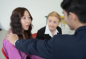 A woman is comforting a young girl. A man is standing behind them. The woman is wearing a purple shirt photo