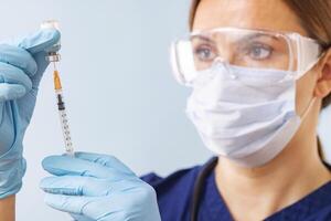 un médico en un protector máscara y lentes llena un jeringuilla con medicina foto