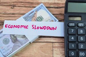 Concept of Economic Slowdown write on sticky notes with dollars isolated on Wooden Table. photo