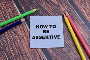 Concept of How to be Assertive write on sticky notes isolated on Wooden Table. photo