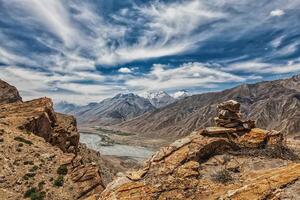 View of valley in Himalayas with stone cairn on cliff photo