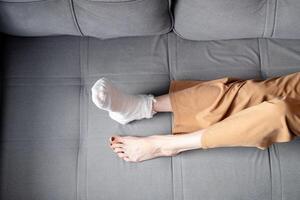 mujer con hermoso, largo piernas y un emitir en su Derecha pierna con muletas mentiras en el sofá, parte superior ver foto