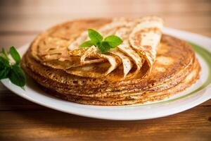 lot of thin pancakes in a plate, on wooden table. photo