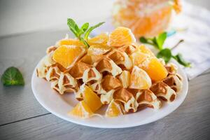 Cooked sweet Belgian waffles with oranges on the table. photo