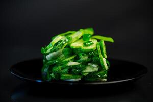 salad of fresh cucumbers with herbs and onions in a plate on a black background. photo