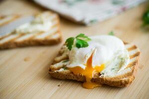 Fried toast bread with spread and poached egg, on a wooden table. photo