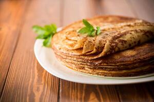 lot of thin pancakes in a plate, on wooden table. photo