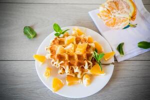Cooked sweet Belgian waffles with oranges on the table. photo