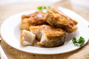 A piece of hake fish fried in a crispy crust, in a plate. photo