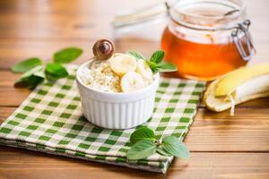 desmoronadizo orgánico cabaña queso con miel y bananas en un cerámico cuenco foto