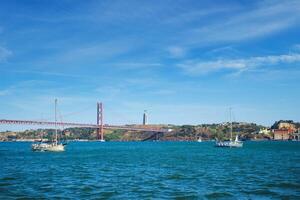 View of 25 de Abril Bridge over Tagus river, Christ the King monument and a yacht boat. Lisbon, Portugal photo