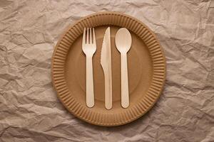 Wooden fork, spoon and knife on cardboard plate on crumpled paper photo